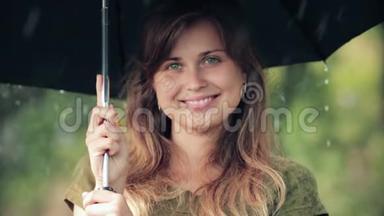 美丽的女人站在雨中的伞下，真诚地笑着，享受大自然
